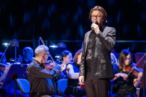 Wokalista Daniel Cebula Oryniczoraz Orkiestra Symfoniczna Filharmonii Podkarpackiej pod batutą Sławomira Chrzanowskiego, w czasie koncertu z piosenkami Zbigniewa Wodeckiego